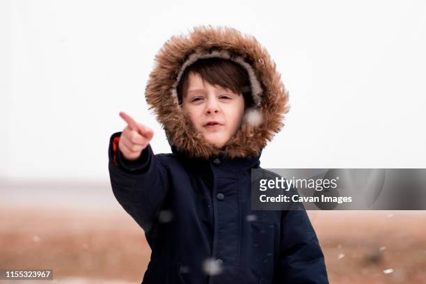 a small young boy pointing at falling snow - parka stock pictures, royalty-free photos & images