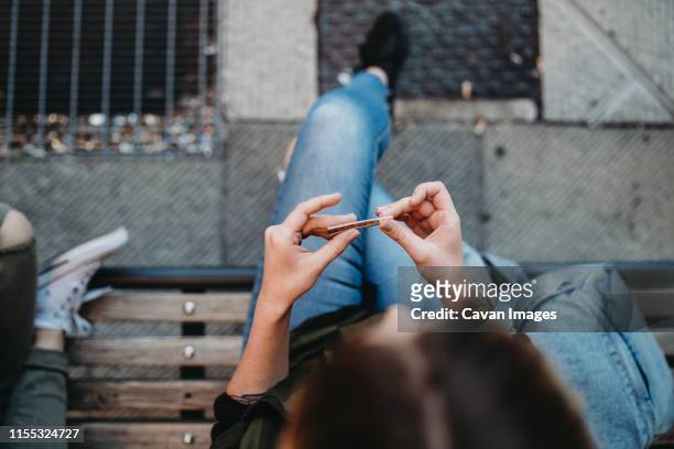 young woman rolling cigarette sitting on the bench - cannabis narcotic stock pictures, royalty-free photos & images