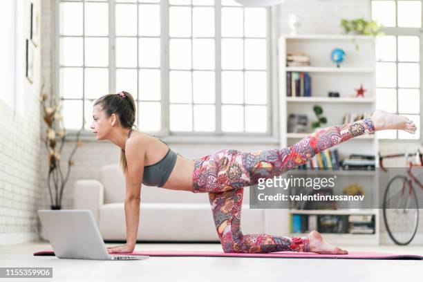 giovane donna sportiva attraente che pratica yoga, facendo esercizio di donkey kick davanti al suo laptop - glutei foto e immagini stock