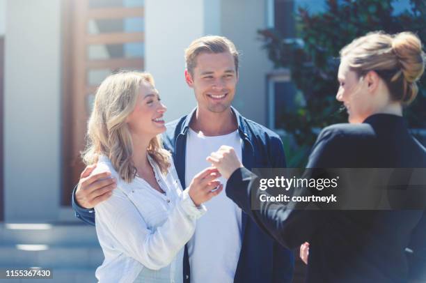 real estate agent giving a young couple the key to their new house. - estate agent sign stock pictures, royalty-free photos & images