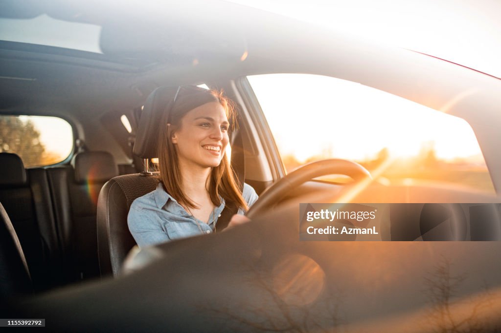 Mulher nova que conduz o carro em um dia ensolarado