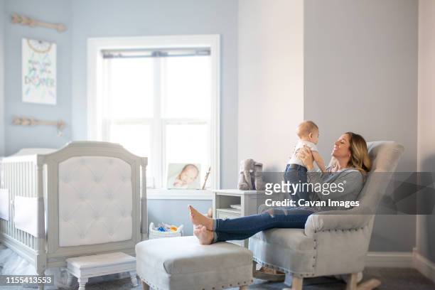 smiling mom holding baby boy in chair in nursery - nursery bedroom stock pictures, royalty-free photos & images