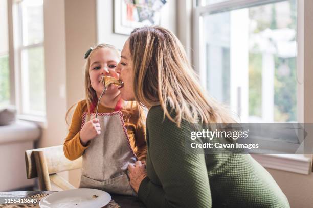 granddaughter feeding pancakes to grandmother at kitchen table - cooking breakfast stock pictures, royalty-free photos & images