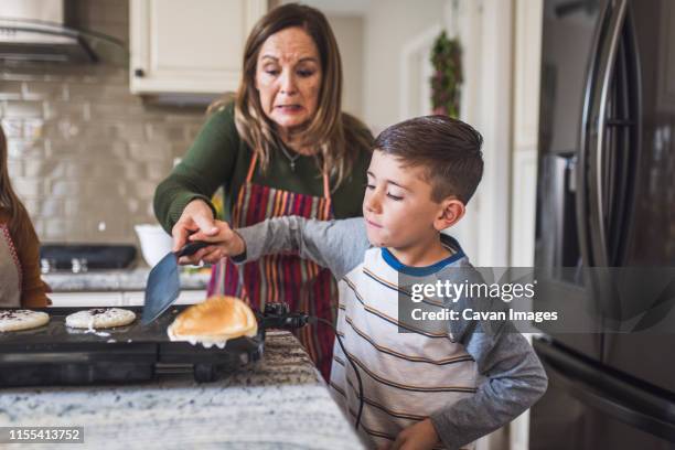 grandson and grandmother flip pancakes, making breakfast in kitchen - basslet stock pictures, royalty-free photos & images