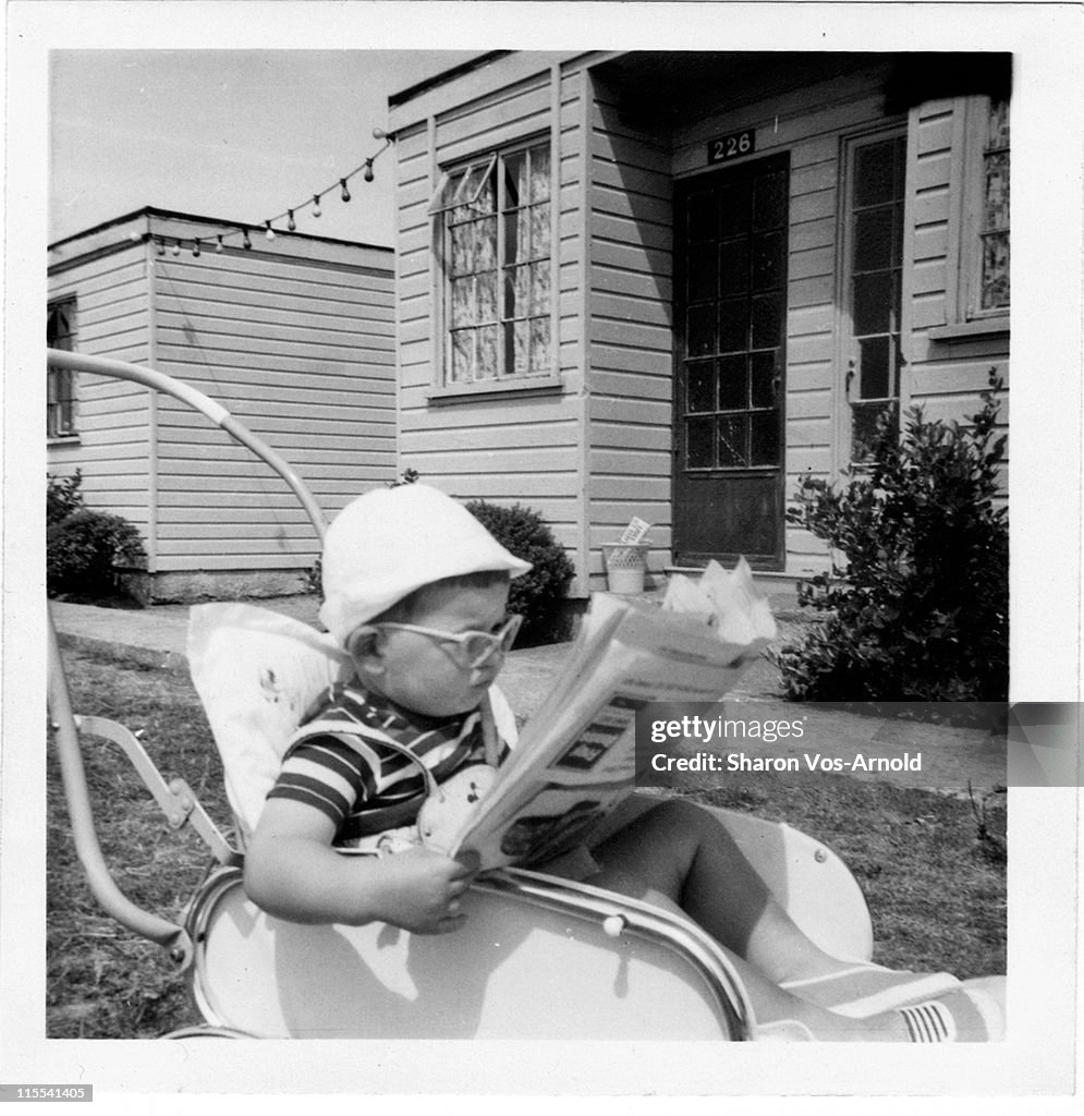 Toddler in his buggy, reading newspaper