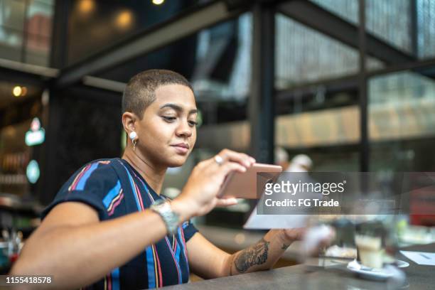 young woman depositing check by phone in the cafe - portable information device stock pictures, royalty-free photos & images
