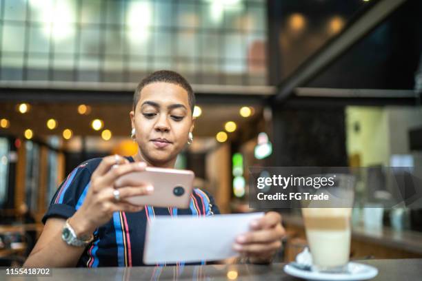 young woman depositing check by phone in the cafe - cheque deposit stock pictures, royalty-free photos & images
