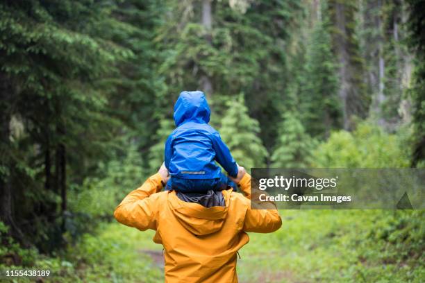 rear view of father carrying son on shoulders during a hike. - wandern regen stock-fotos und bilder