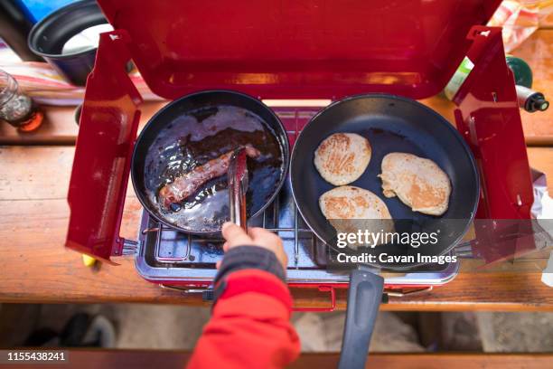 female camper cooking pancakes and bacon at her campsite. - camping stove stockfoto's en -beelden