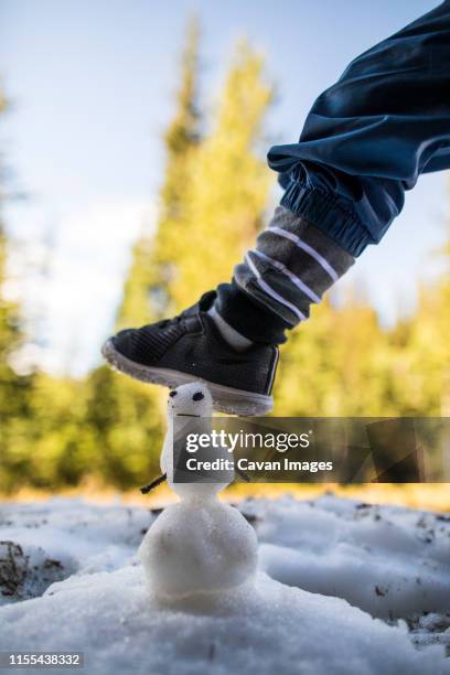 toddler boy stepping on miniature snowman. - melting snowball stock pictures, royalty-free photos & images