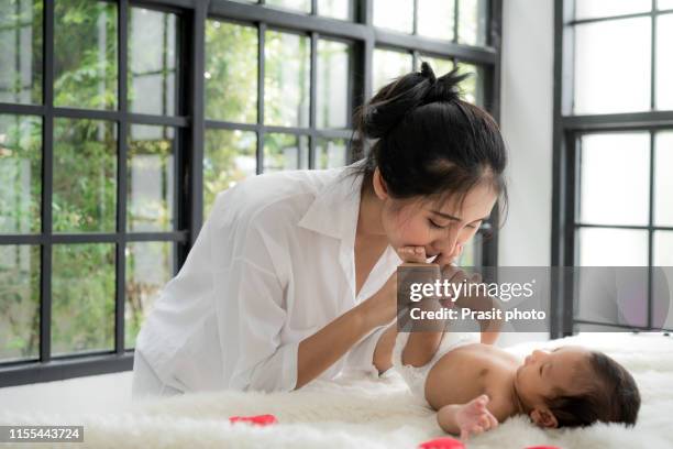 asian happy young mother kissing her two months old daughter's feet in bed at home - new mum stock-fotos und bilder