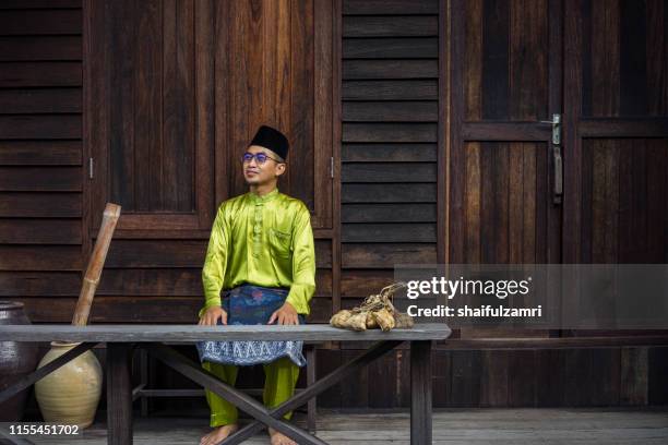 a malay man in malay traditional cloth showing his happy reaction during hari raya celebration. - hari raya celebration stock-fotos und bilder