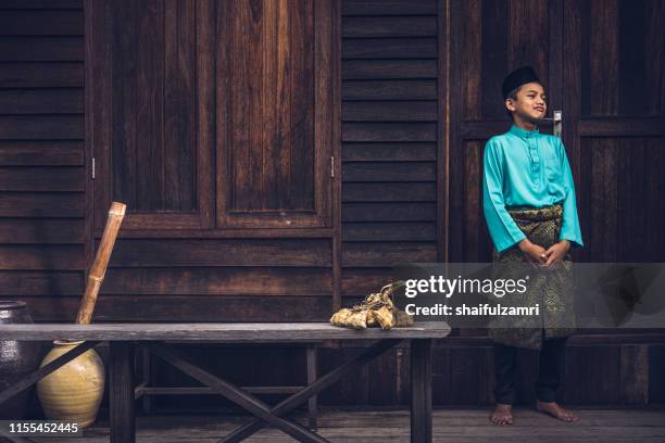 a malay boy in malay traditional cloth showing his happy reaction during hari raya celebration. - hari raya celebration stock-fotos und bilder