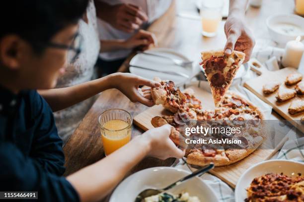 group of joyful young asian man and woman having fun, passing and sharing food across table during party - pizza restaurant stock pictures, royalty-free photos & images