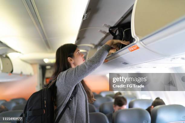 woman putting luggage in overhead bin in airplane - carry on bag imagens e fotografias de stock