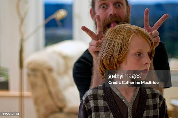 father pulling faces behind his sons head - veralbern stock-fotos und bilder
