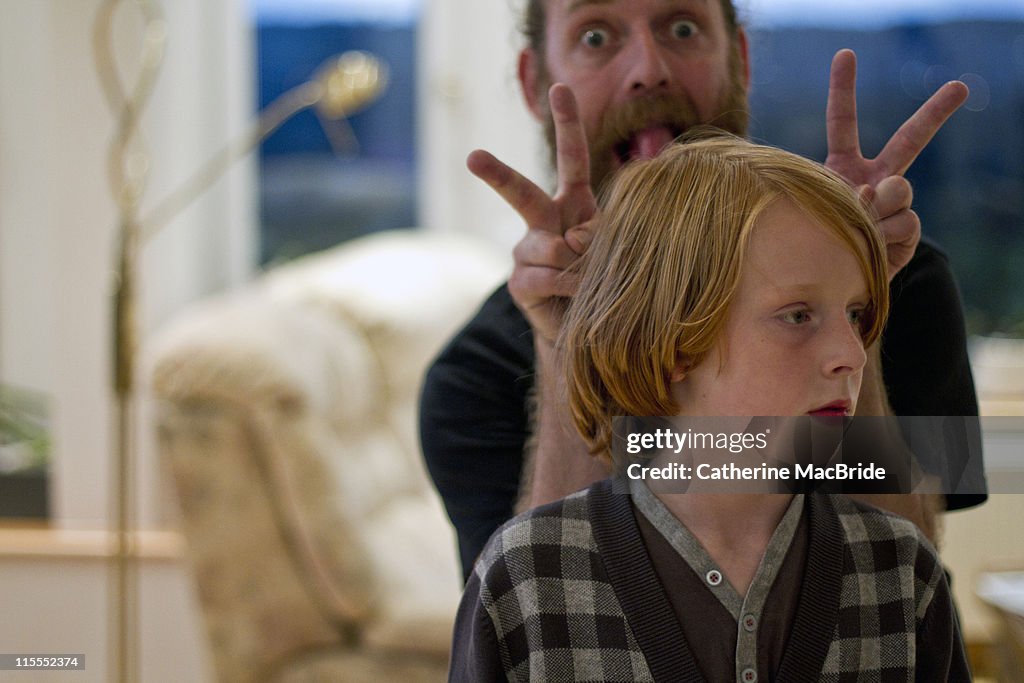 Father pulling faces behind his sons head