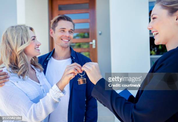 real estate agent giving a young couple the key to their new house. - handing over keys stock pictures, royalty-free photos & images
