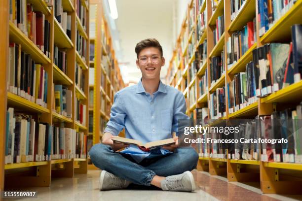 smiling teenage boy in library - teenager reading a book stock pictures, royalty-free photos & images