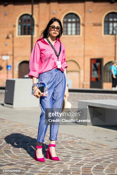 Guest, wearing a neon pink shirt, blue pants, fuchsia heels and holographic bag, is seen during Pitti Immagine Uomo 96 on June 12, 2019 in Florence,...