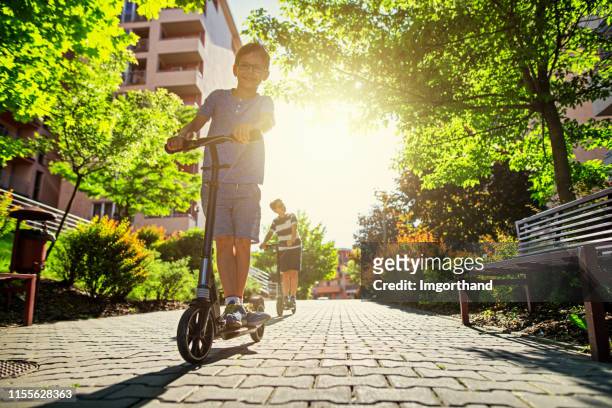 kids riding scooters in city residential area. - street style stock pictures, royalty-free photos & images