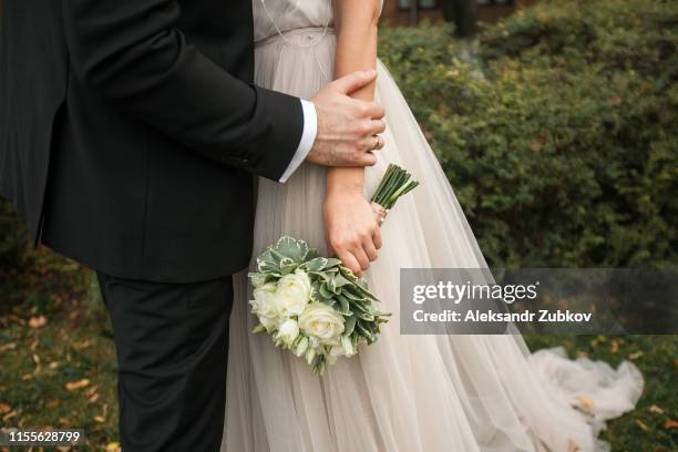 the bride is holding a beautiful bouquet of white roses and green leaves. embrace the newlyweds, the hands of the bride and groom close-up. wedding theme - man holding engagement ring stock pictures, royalty-free photos & images