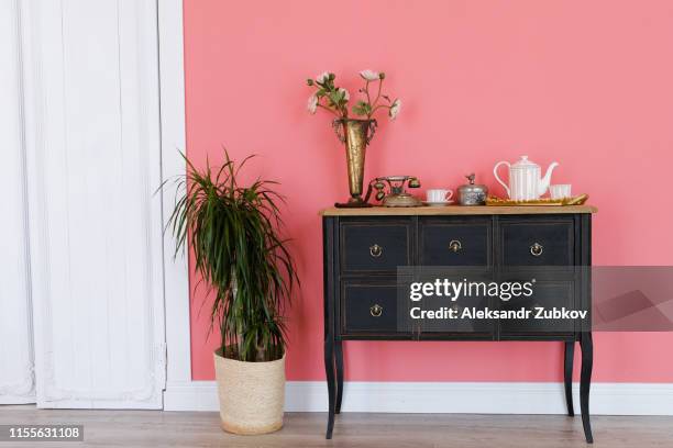 old chest of drawers with objects on the background of a pink wall. next flower in a pot, white door. beautiful interior in vintage style. - antique furniture stock pictures, royalty-free photos & images