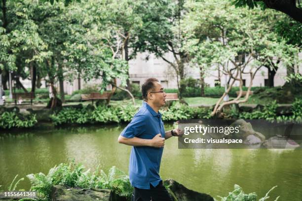 senior man jogging by lake at park - running man profile stock pictures, royalty-free photos & images