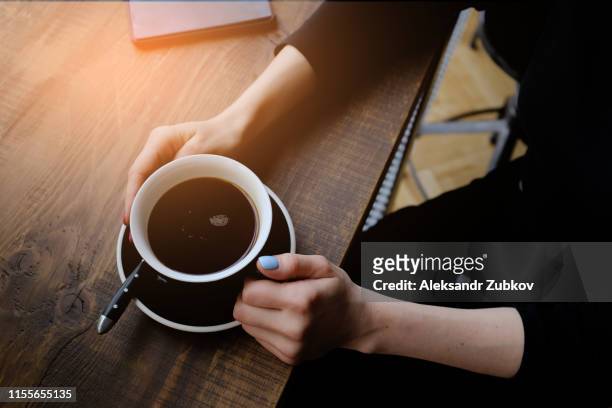 the girl holds a cup of coffee on a wooden table in the cafe. near the phone. coffee-break. the concept of food, business, entrepreneurship. - coffee top view stock-fotos und bilder