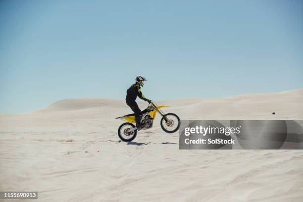 motorradfahrer zieht ein rad auf den sand - wheelie stock-fotos und bilder