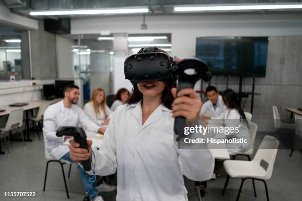 group of students doing research while female student experiments with virtual reality goggles - virtual reality classroom stock pictures, royalty-free photos & images