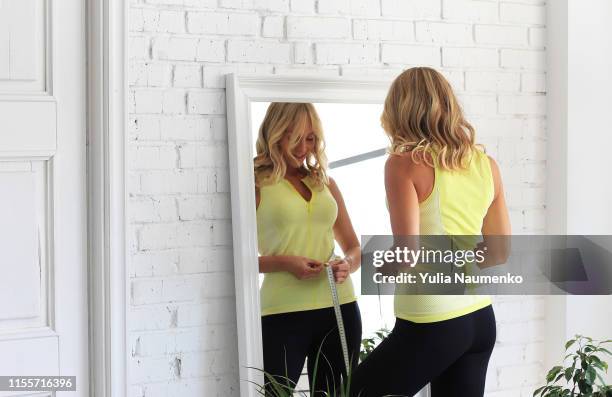 stay in shape. young woman with athletic body measures her waist with a measure type in front of a mirror. - thin ribbon stock pictures, royalty-free photos & images