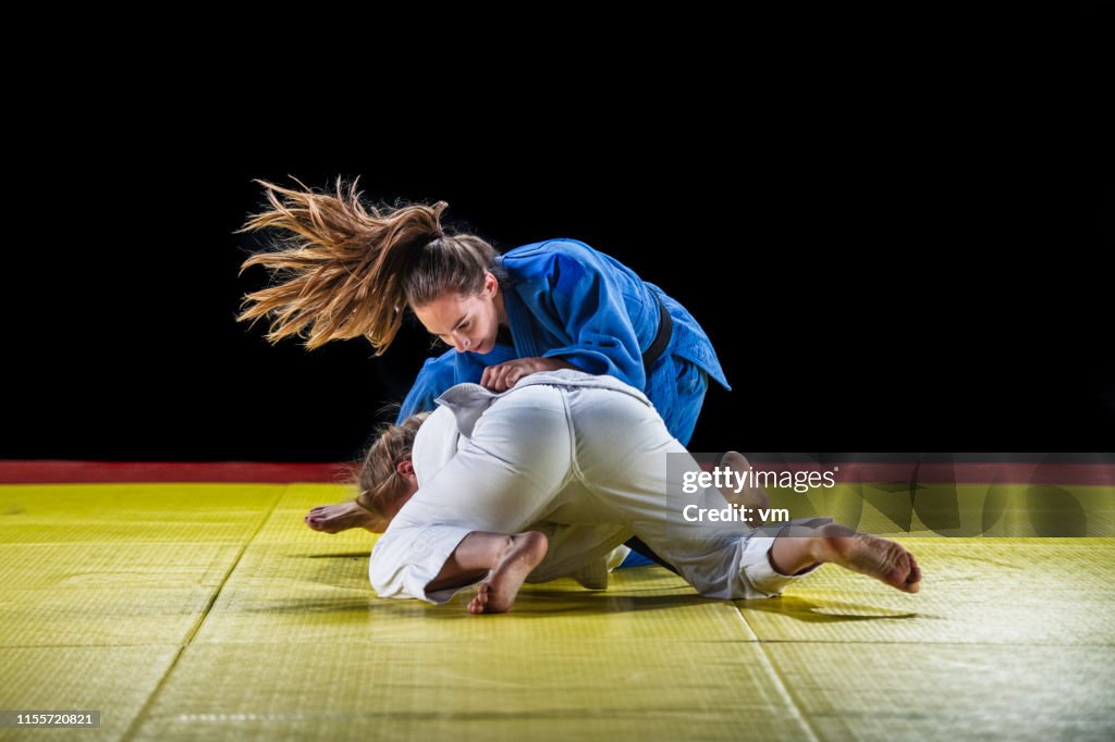 Two female judo practitioners grappling on a tatami mat
