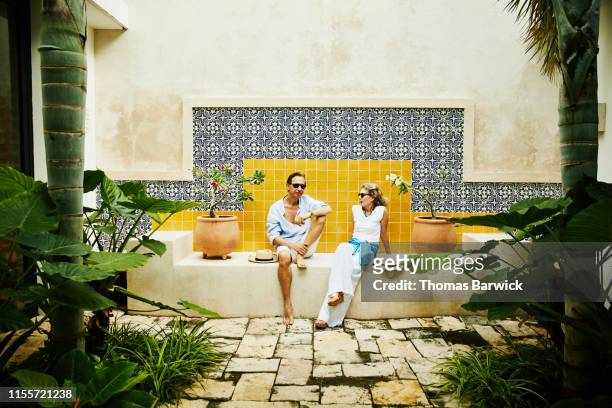 portrait of senior couple relaxing in courtyard at tropical resort - wisdom stock pictures, royalty-free photos & images