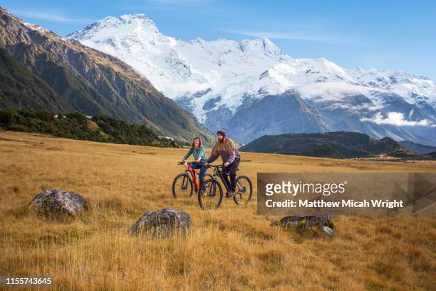 friends ride mountain bikes through the mount cook national park. - mount cook stock pictures, royalty-free photos & images
