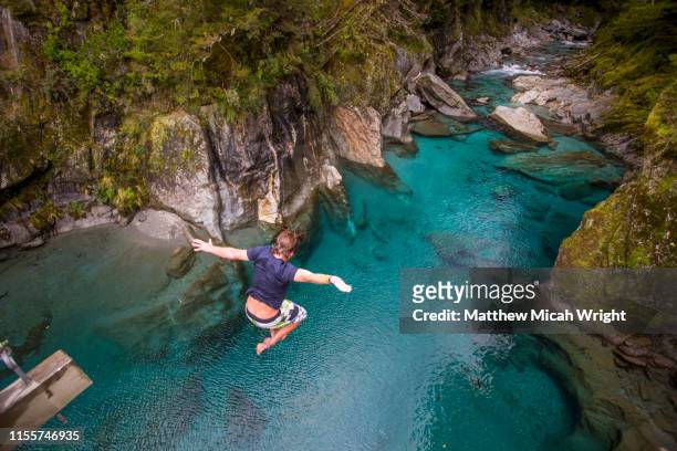 the blue pools of makarora offer enticing blue waters to swim in. a man jumps off a bridge into the water. - new zealand travel stock pictures, royalty-free photos & images
