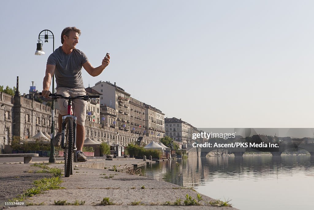 Man bicycles along river edge, checks text