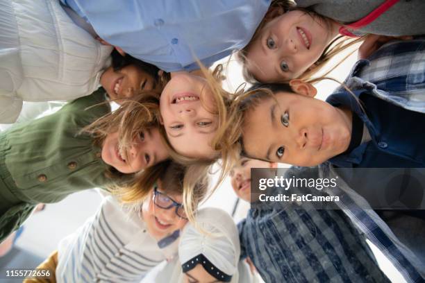 an adorable group of diverse kids look down at camera while huddled together - summer school stock pictures, royalty-free photos & images