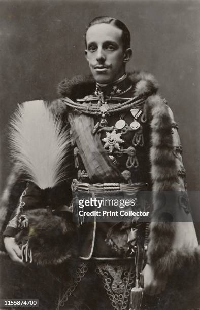 King of Spain', circa 1910. Portrait of Alfonso XIII , King of Spain, wearing a fur-lined cape and holding a plumed helmet. The posthumous son of...