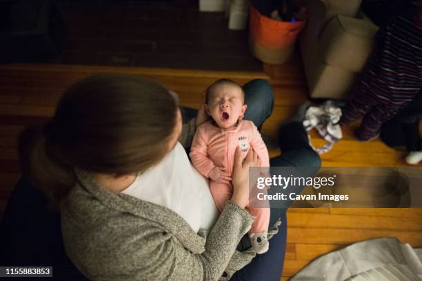 mother holding infant daughter yawns while sitting on beanbag indoors - new mum stock-fotos und bilder