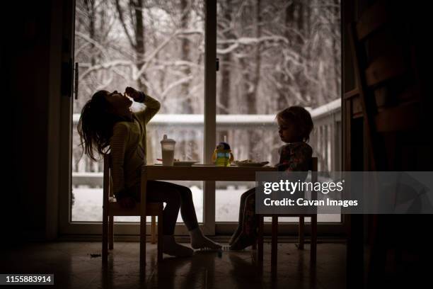 sisters eating in front of window with snowy view - winter breakfast stock pictures, royalty-free photos & images