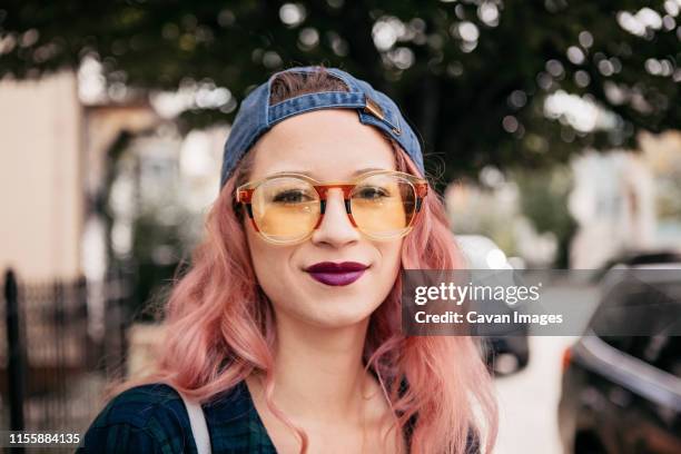 young millennial strolls downtown street in yellow sunglasses - lila lippenstift stock-fotos und bilder