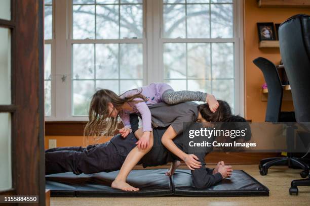 a father holds a plank position with two children piled on his back - family yoga stock pictures, royalty-free photos & images