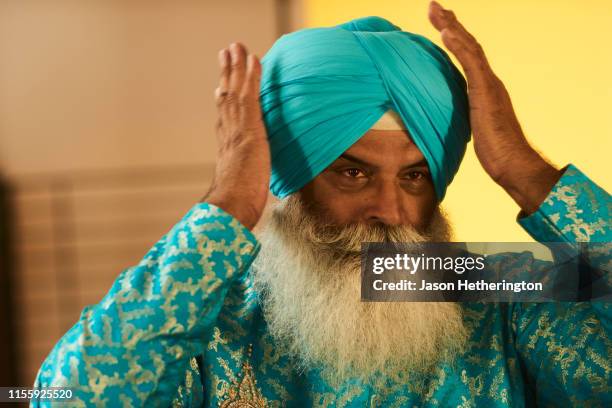 a senior sikh man adjusting his turban - turban stock pictures, royalty-free photos & images