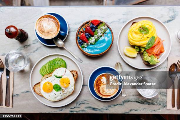 brunch at cafe with avocado toast, fried and scrambled egg, salmon, smoothie bowl and coffee - breakfast table stock pictures, royalty-free photos & images