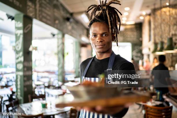 serious male chef holding prepared dish at restaurant - black chef stock pictures, royalty-free photos & images