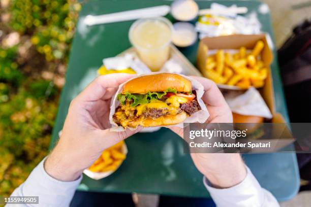 man eating cheeseburger, personal perspective view - fastfood restaurant table stock-fotos und bilder