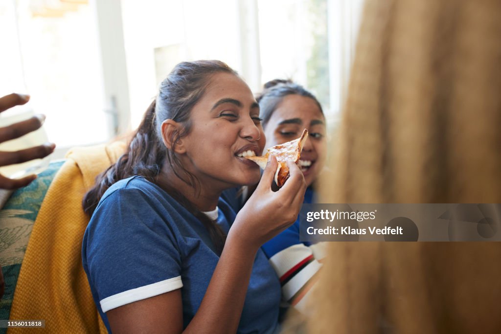 Cheerful young woman eating slice of pizza