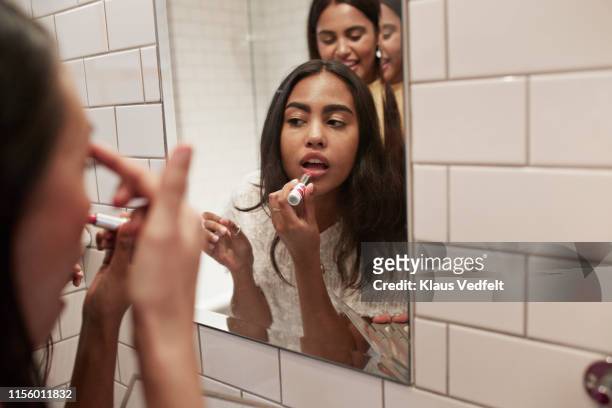 woman applying lipstick while reflecting in mirror - woman lipstick rearview stock-fotos und bilder