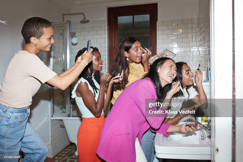 Smiling woman photographing friends doing make-up